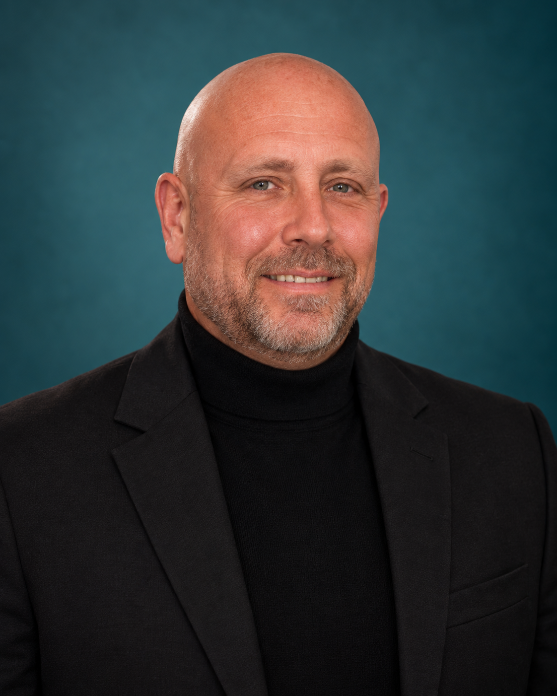 Ron Devine smiling in a black jacket and turtleneck against a teal background